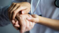 Eine Pflegekraft hält die Hand eines älteren Menschen.