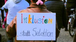 Eine Demonstrantin hat ein Schild auf dem Rücken, auf dem steht: "Inklusion statt Selektion".